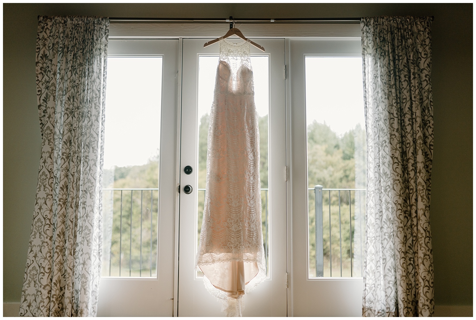 Boho cream lace sheath style wedding dress is hanging up in a three panel window.