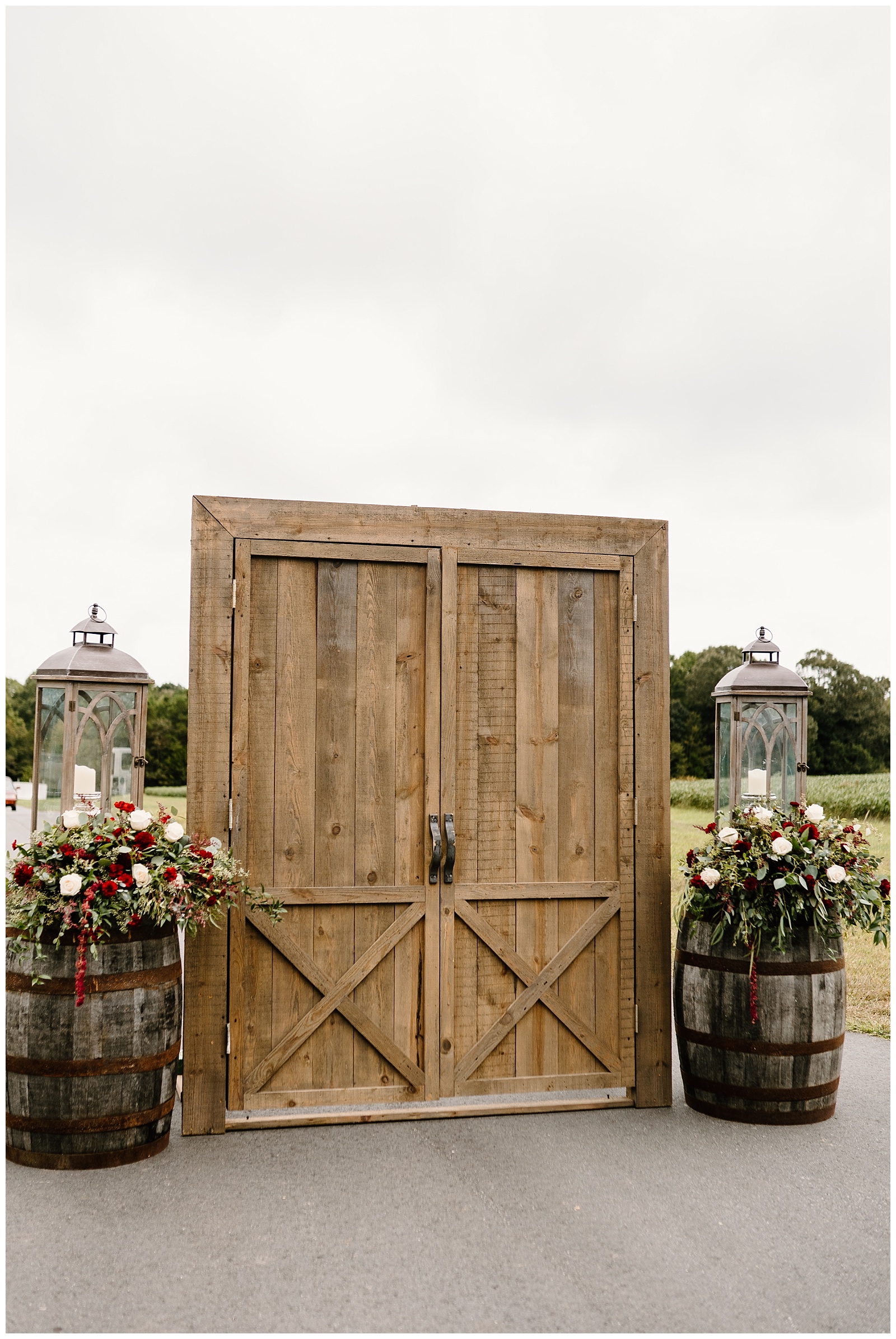 Barn door style entrance arch for the wedding aisle Rustic barrel wedding decoration with large bouquet of greenery, dark bordeaux mums, and dusty pink roses.