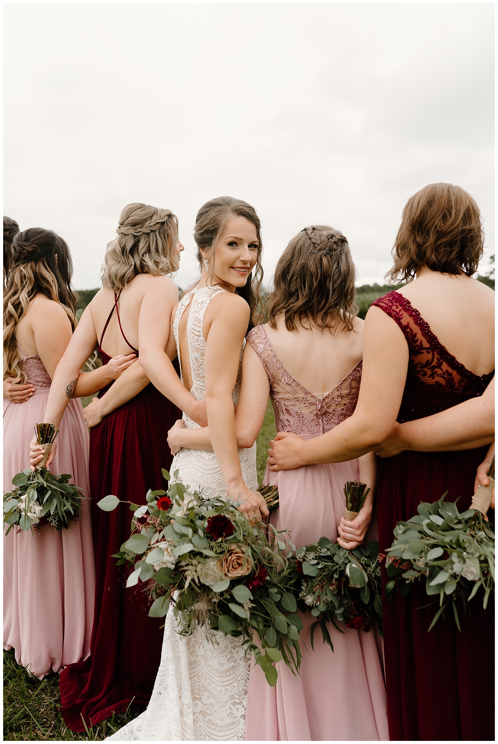 Bridesmaids turn around to show off the details on their low cut back dresses. The bride is turned around looking over her shoulder at the camera.