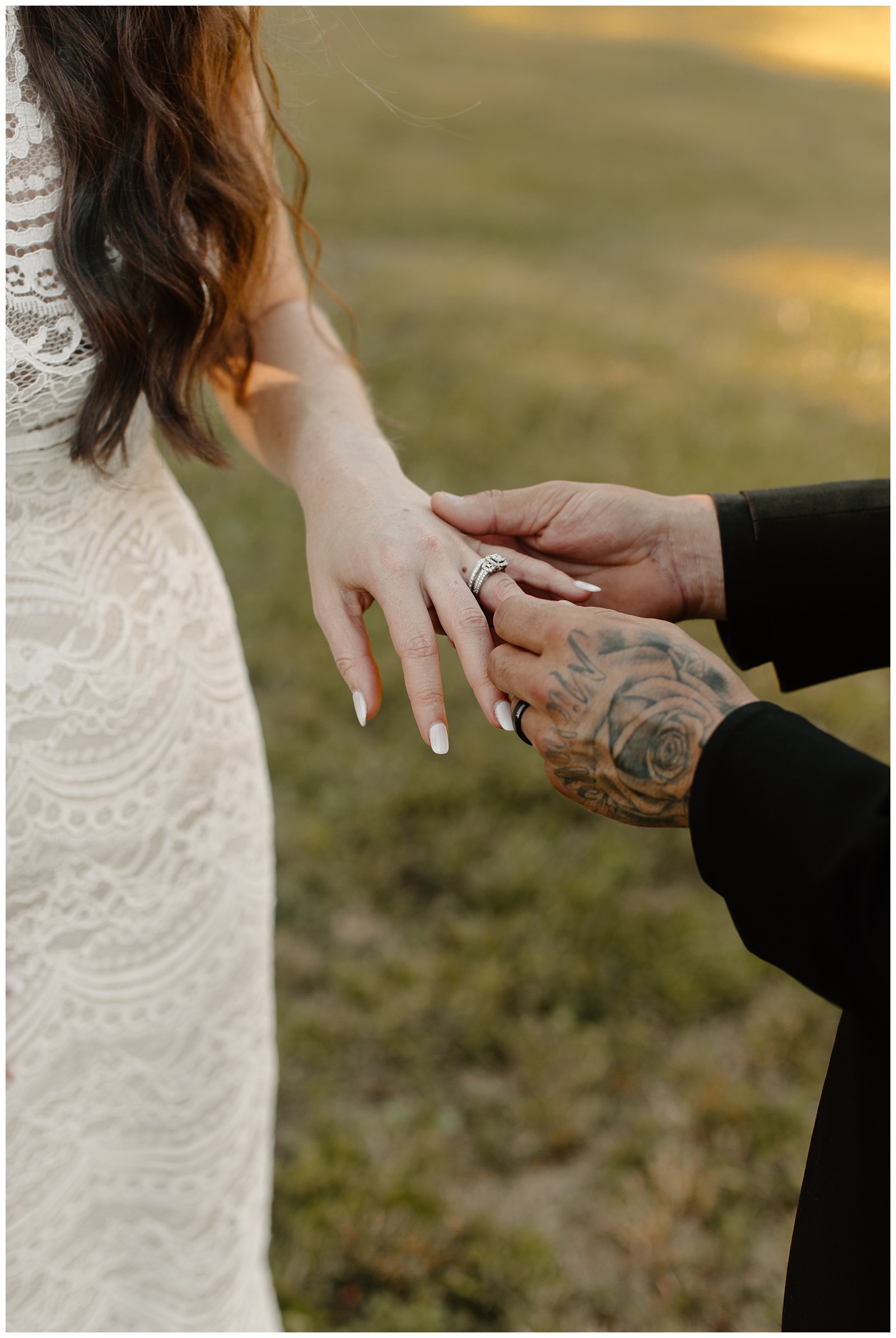 Romantic sunset portrait of newlywed couple showing off engagement and wedding rings with hand tattoos showing