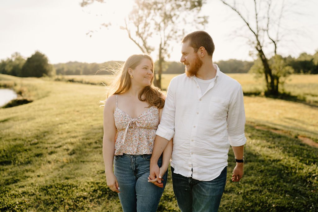 Couple holding hands in open field in North Carolina with golden hour light 
